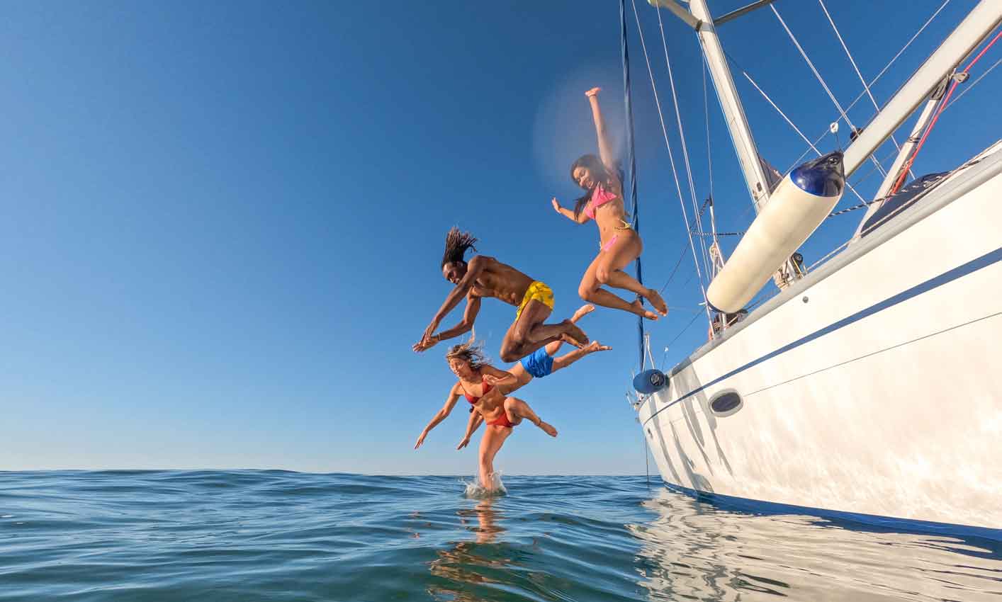 friends jumping out of a boat in the sea while having fun during their summer vacation