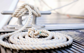 Close-up of a mooring rope with a knotted end tied around a cleat on a wooden dock