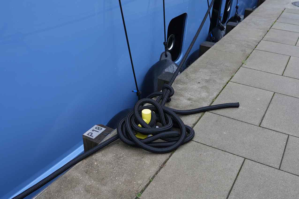 black mooring rope with yellow end coiled on concrete dock beside blue boat hull