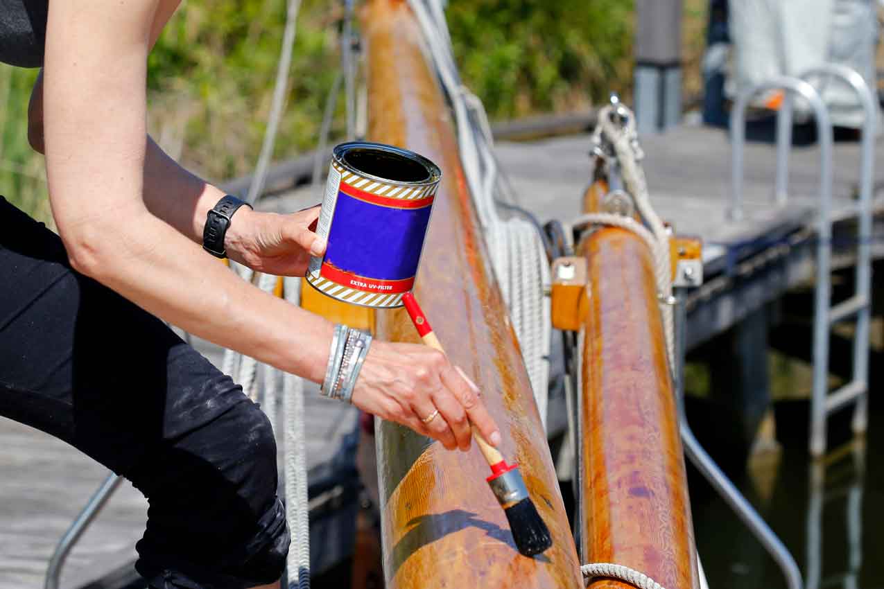 A young woman varnishing the wooden mast of a classic sailing yacht